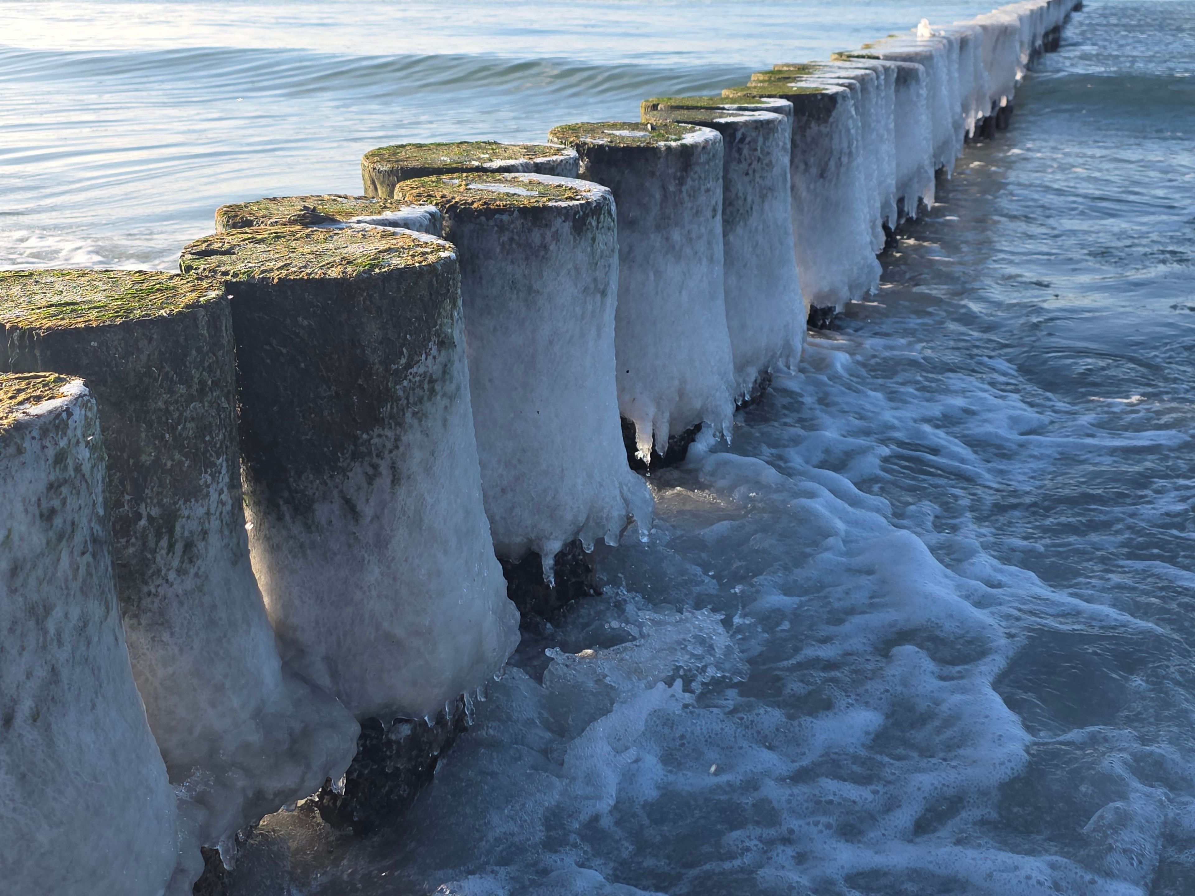 A row of concrete sea defense structures with ice formations.