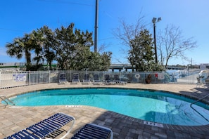 A swimming pool with lounge chairs, a lifeguard sign, and a shallow water warning sign. - Riverfront condo w Open & Screened-In Porches with Water & Marsh Views and Community Pool (Folly Beach)