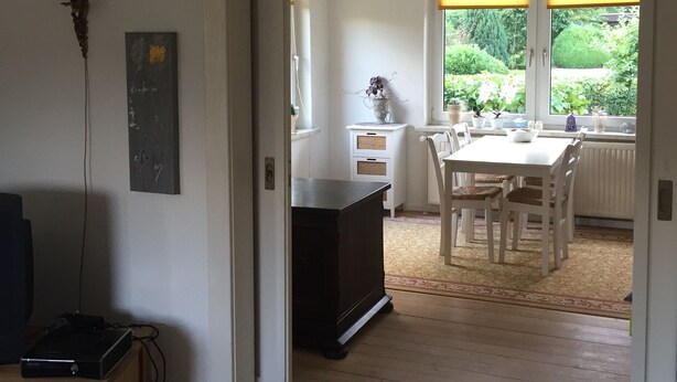 Una habitació amb terra de fusta, una taula de dinar amb cadires, un armari blanc i una finestra amb persianes.