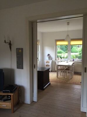 A room with a wooden floor, a dining table with chairs, a white cabinet, and a window with blinds. - Romantic holiday home detached on a large plot (Plau-Plötzenhöhe)