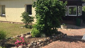 Una casa amb teules vermelles, una xemeneia de maó i un jardí amb plantes diverses i un camí de maó.