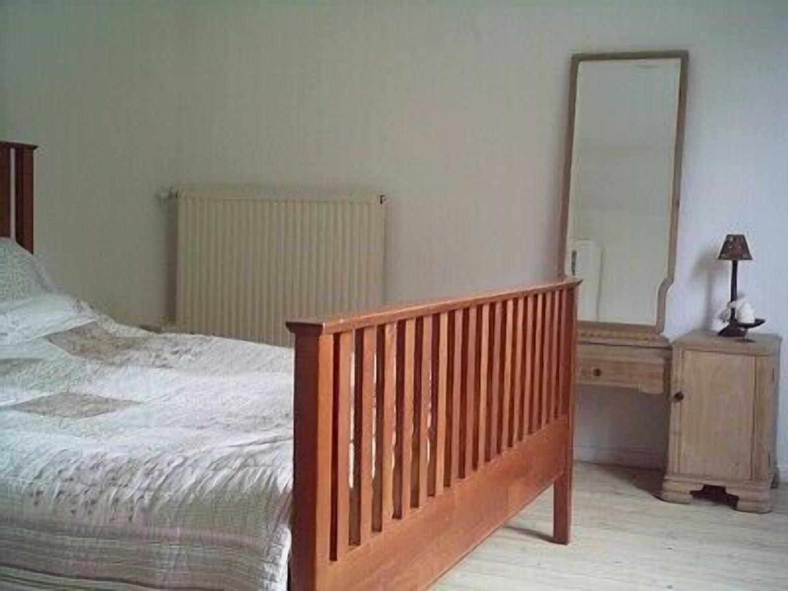 Un dormitorio con una cama de madera, una mesita de noche, un espejo y un radiador.