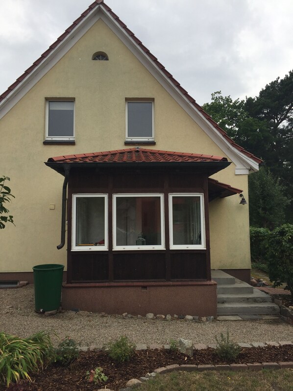 A two-story house with a sloped roof, a front porch with a bench, and a small garden area. - Romantic holiday home detached on a large plot (Plau-Plötzenhöhe)