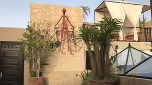 A courtyard with a large wall-mounted sculpture, potted plants, a bicycle, and a black gate. - RIAD L'EMPIRE in the heart of the MEDINA (Marrakech)