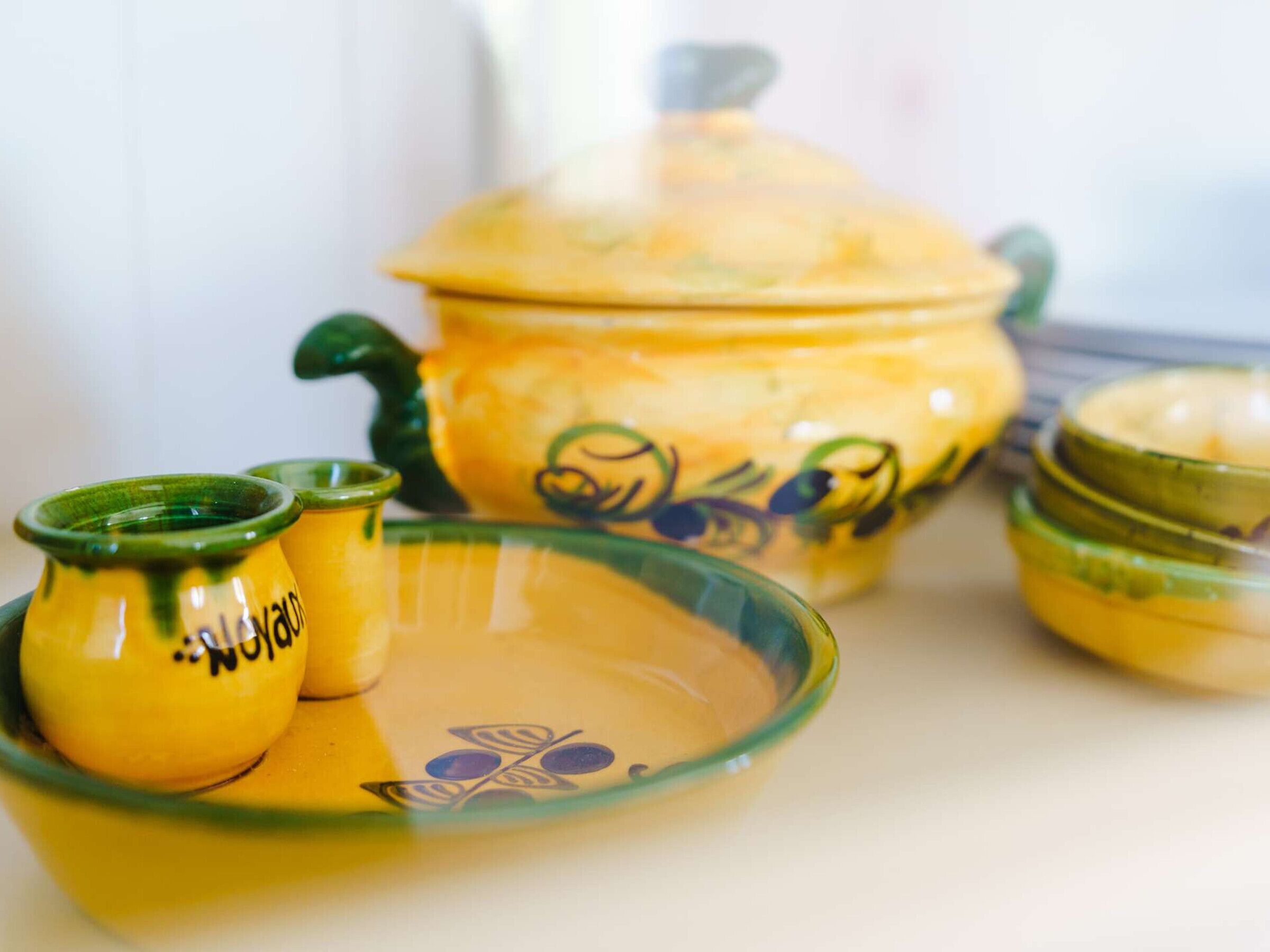 Conjunto de utensílios de cozinha em cerâmica amarela com detalhes em verde, incluindo uma panela, uma tigela e duas xícaras pequenas.