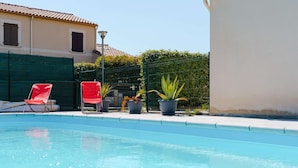 Una piscina con dos sillones rojos y plantas en macetas.