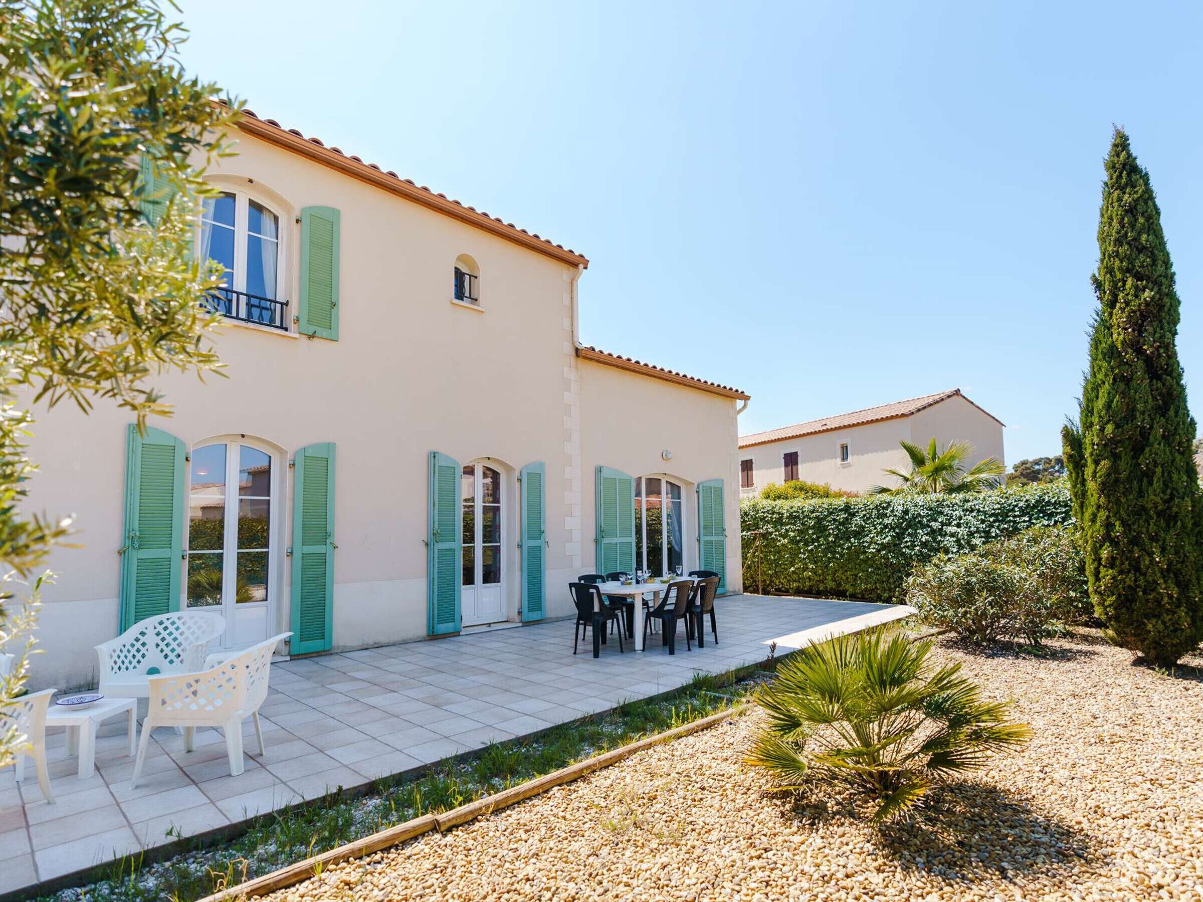 A two-story house with a tiled patio, outdoor furniture, and a well-maintained garden.