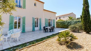 Una casa de dos pisos con un patio empedrado, mobiliario exterior y un jardín bien cuidado.