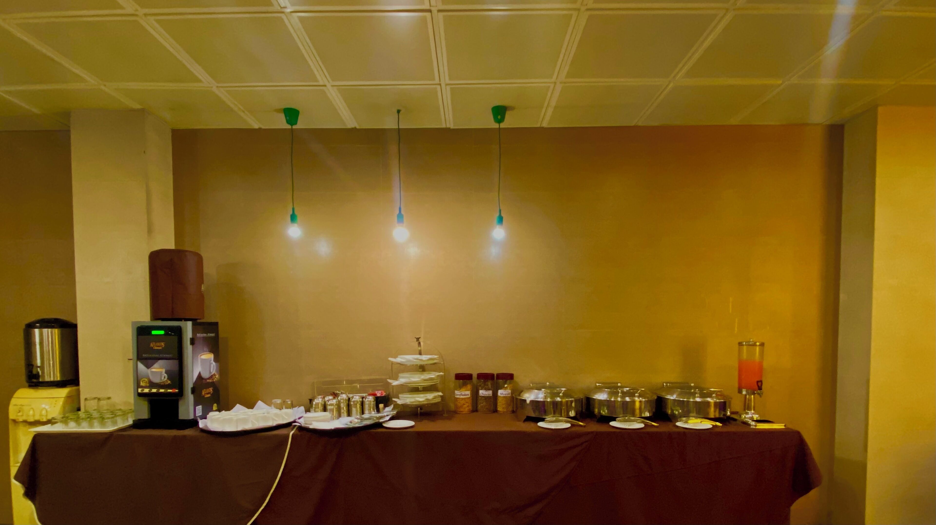 Una mesa con un sistema de buffet que incluye una máquina de café, un dispensador de bebidas y varios recipientes con alimentos.