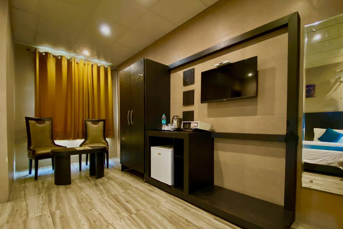 A hotel room with a bed, a TV, a small fridge, a desk with a chair, and a large mirror.