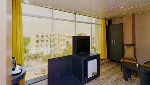 A hotel room with a large window, a television, a small refrigerator, a desk, and a cabinet. - Ace Prime Hotel (Greater Noida)