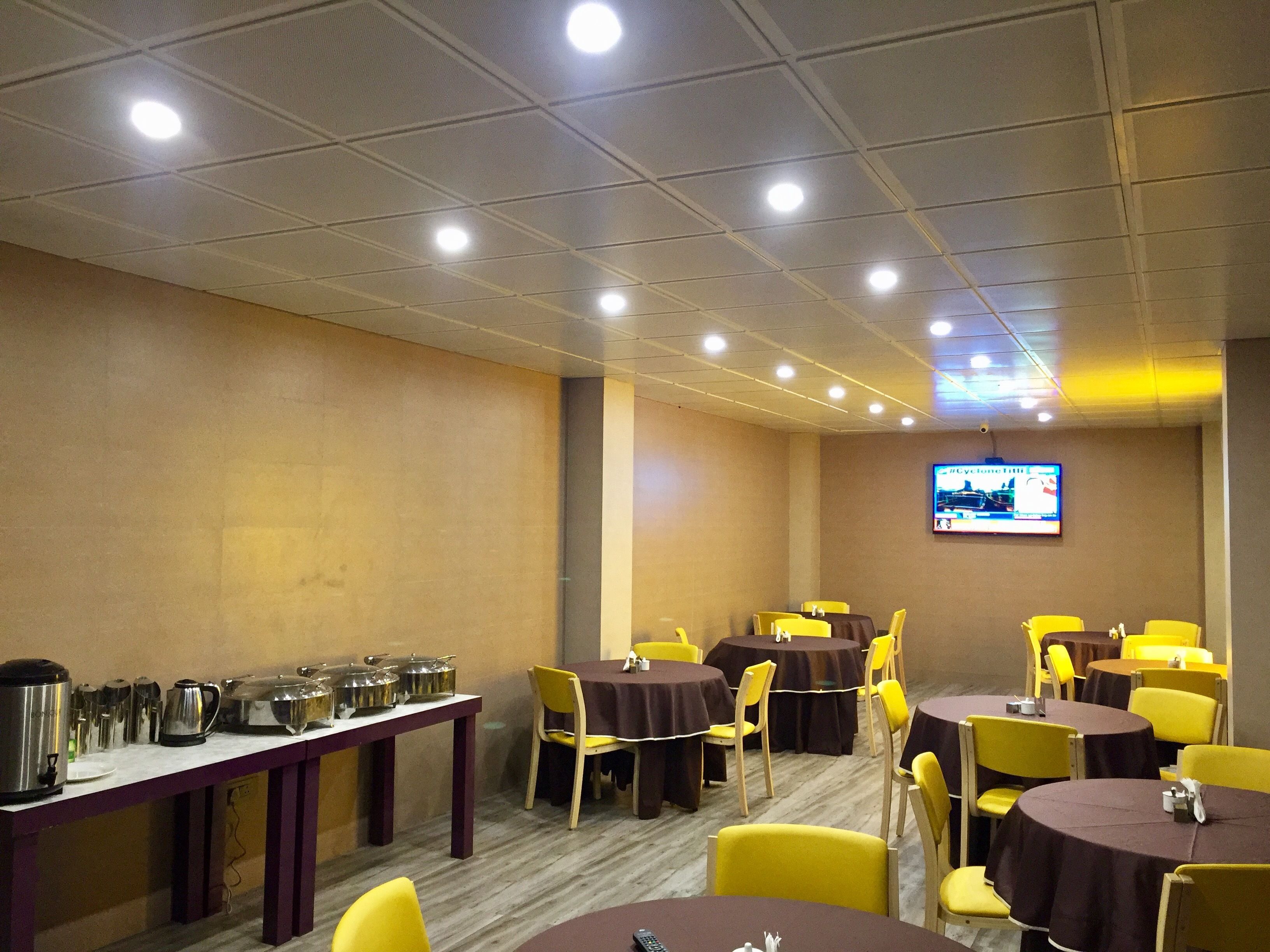 Un salón de conferencias con varias mesas y sillas, equipado con una estación de café y una pantalla de televisión que muestra un noticiero.