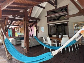 A spacious covered deck with a hammock, wicker furniture, and a dining area. - Wooden villa with private pool in a tropical garden 3 minutes from the beach (Sainte-Anne)