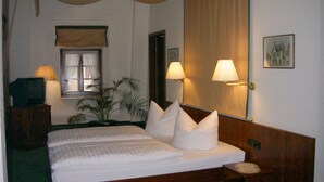 Une chambre d’hôtel avec un lit, deux lampes de chevet, une table de nuit, une fenêtre avec des rideaux, un miroir et un tableau encadré au mur.