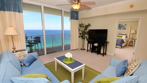 A living room with a sofa set, a coffee table, a TV, and a balcony with a view of the ocean. - BOOK SUMMER NOW. GREAT RATES! Gulf-Front Master w/Balcony + PRIVATE Bunkroom (Panama City Beach)