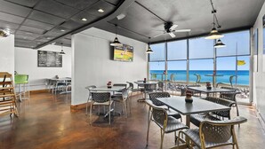 A spacious indoor area with tables and chairs, large windows offering a view of the sea, and a ceiling fan. - BOOK SUMMER NOW. GREAT RATES! Gulf-Front Master w/Balcony + PRIVATE Bunkroom (Panama City Beach)