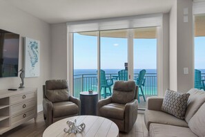 A spacious living room with a large sliding glass door leading to a balcony with ocean views. There are two leather armchairs, a round coffee table, and a beige sofa. - 3 bed 3 bath -Luxury Gulf-Front Escape + Beach Chairs & Topgolf (Panama City Beach)