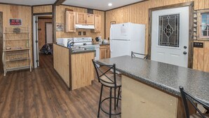 A compact kitchen with wooden cabinets, a built-in stove, a refrigerator, and a bar stool. - Mid- Lake home, perfect for a group w/ lots of boat and truck parking (Scottsboro)