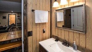 A bathroom with wooden paneling, a white sink, a vintage-style faucet, and a mirror with a wooden frame. - Mid- Lake home, perfect for a group w/ lots of boat and truck parking (Scottsboro)