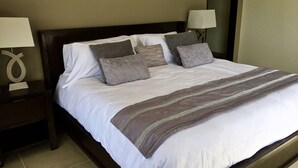 A neatly made bed with white linens and multiple pillows, a dark wooden headboard, and two bedside lamps on matching nightstands. - Amazing Ocean view  !!! (Potrero)