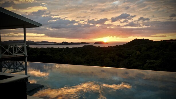 Una piscina infinita con vista a la puesta de sol sobre un paisaje montañoso.