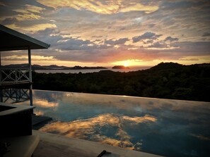 Una piscina infinita con vista a la puesta de sol sobre un paisaje montañoso.