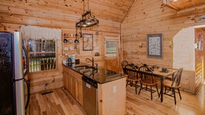 A wooden cabin interior with a kitchen, dining area, and a window overlooking a deck. - Highland Dream, Hot Tub, FREE tickets each paid day, Near Dollywood, WIFI!!! (Sevierville)
