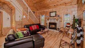 A log cabin interior with a fireplace, wooden floors, a black leather sofa, a wooden rocking chair, and a staircase. - Highland Dream, Hot Tub, FREE tickets each paid day, Near Dollywood, WIFI!!! (Sevierville)
