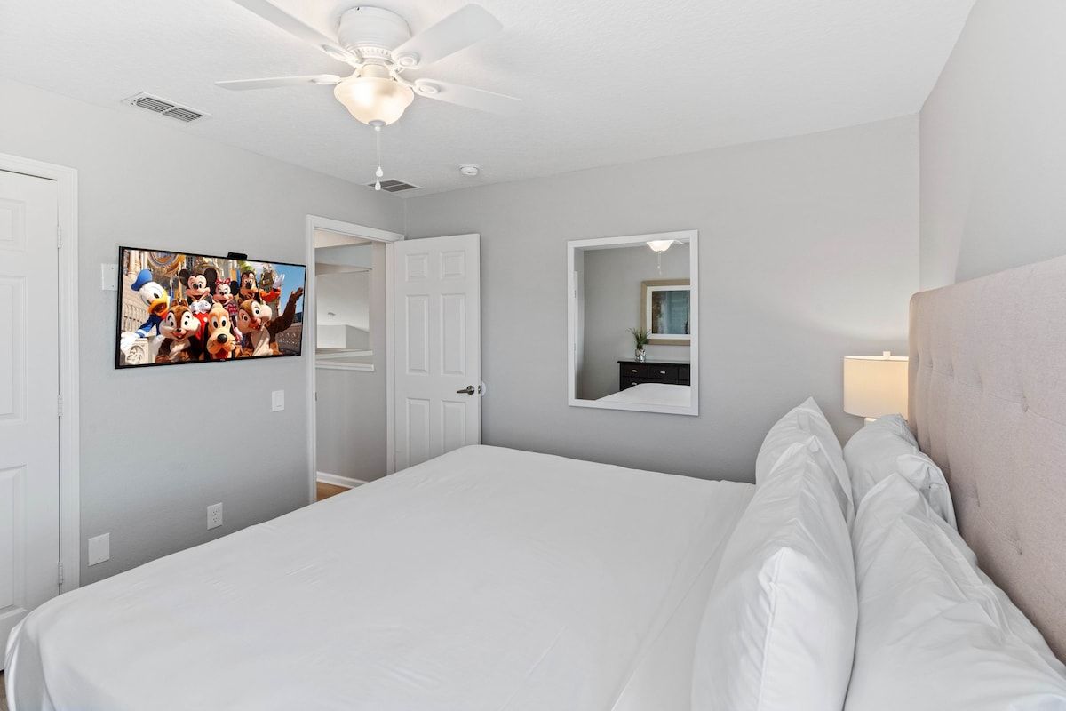 A hotel room with a bed, a ceiling fan, a television on the wall, and a mirror.