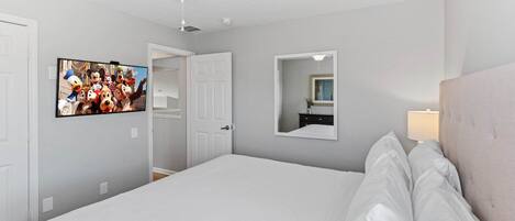 A hotel room with a bed, a ceiling fan, a television on the wall, and a mirror.