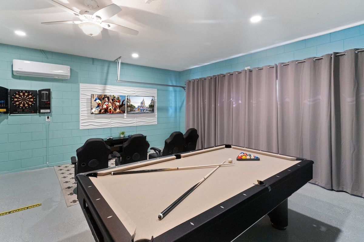 A pool table with cue sticks, a dartboard, and a framed photo on the wall.