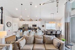 A modern living room with a sofa, dining area, kitchen, and a staircase.
