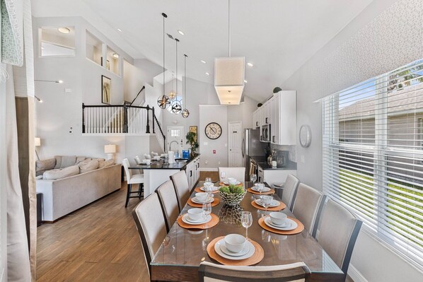 Un espace repas moderne avec une table en bois disposée pour six personnes, entourée de chaises. Un escalier avec une rampe mène à un niveau supérieur.