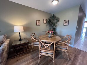 A dining area with a round table, four chairs, a lamp, and framed pictures on the wall.