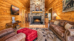 L’intérieur d’une cabane en rondins, avec une cheminée en pierre, des murs en bois, un pouf rouge et des canapés en cuir.