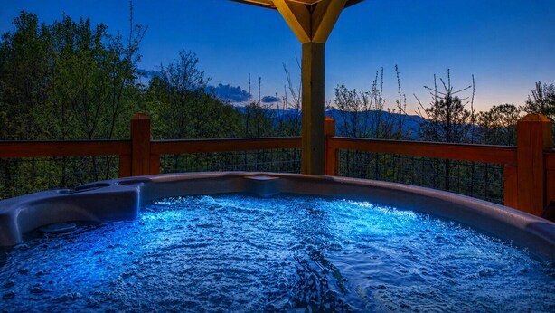 Un bain à remous sous une pergola en bois, avec vue sur les arbres et les montagnes.
