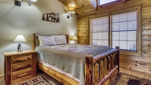 Une chambre à coucher dans un chalet en bois, avec un lit, deux lampes fixées au mur, une table de chevet et une fenêtre avec des stores.