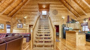 A wooden interior with a central staircase, a living area with a sofa, and a kitchen area. - Big Sky, Breathtaking Mtn View, Free Attraction Tickets, Pool Table, Hot Tub!!! (Sevierville)