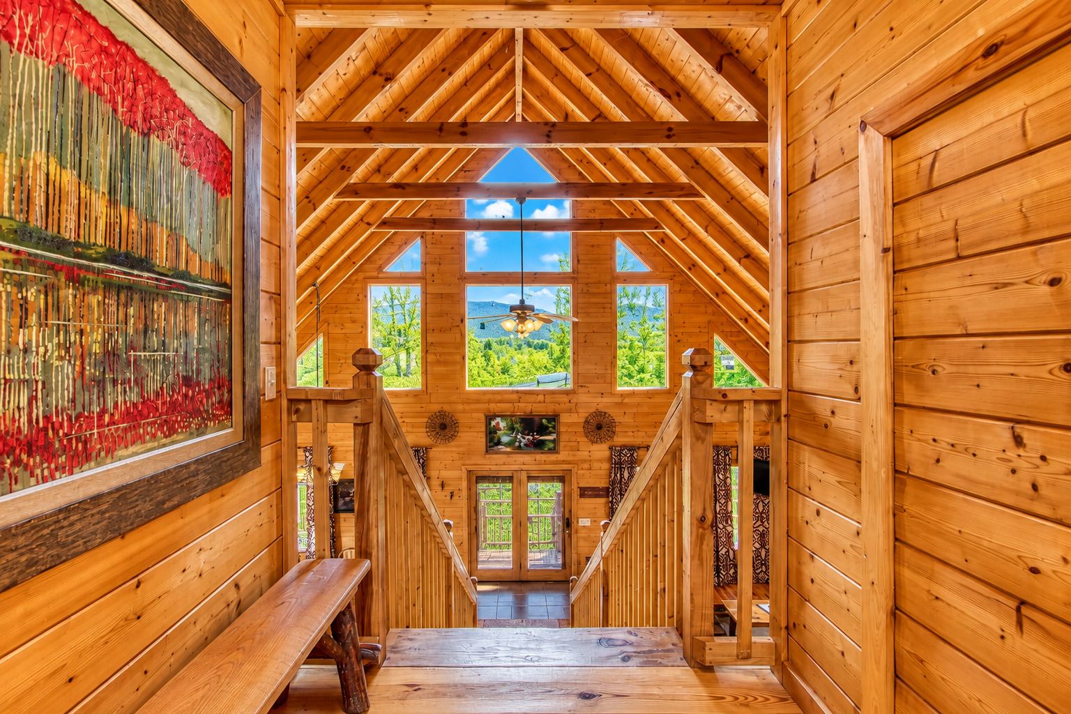 A wooden interior with a staircase leading to a door, a large window, and a wall-mounted painting.
