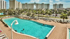 A hotel with a large swimming pool, palm trees, and a view of high-rise buildings.