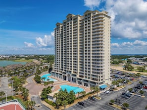 A high-rise hotel with multiple balconies, a swimming pool, and a parking lot.