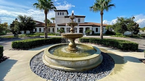 A circular fountain with water spouting from the top, surrounded by a pebble border, with palm trees and a white building in the background. - Lazy River! VALUE PRICED! Waterpark Adventure Resort Near Disney! 2018 (Kissimmee)