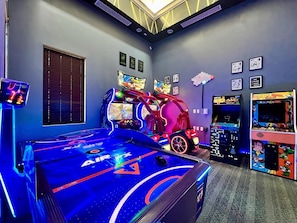 Ein Spielzimmer mit Billardtisch, Spielautomaten und einer neonbeleuchteten Rennsimulation.