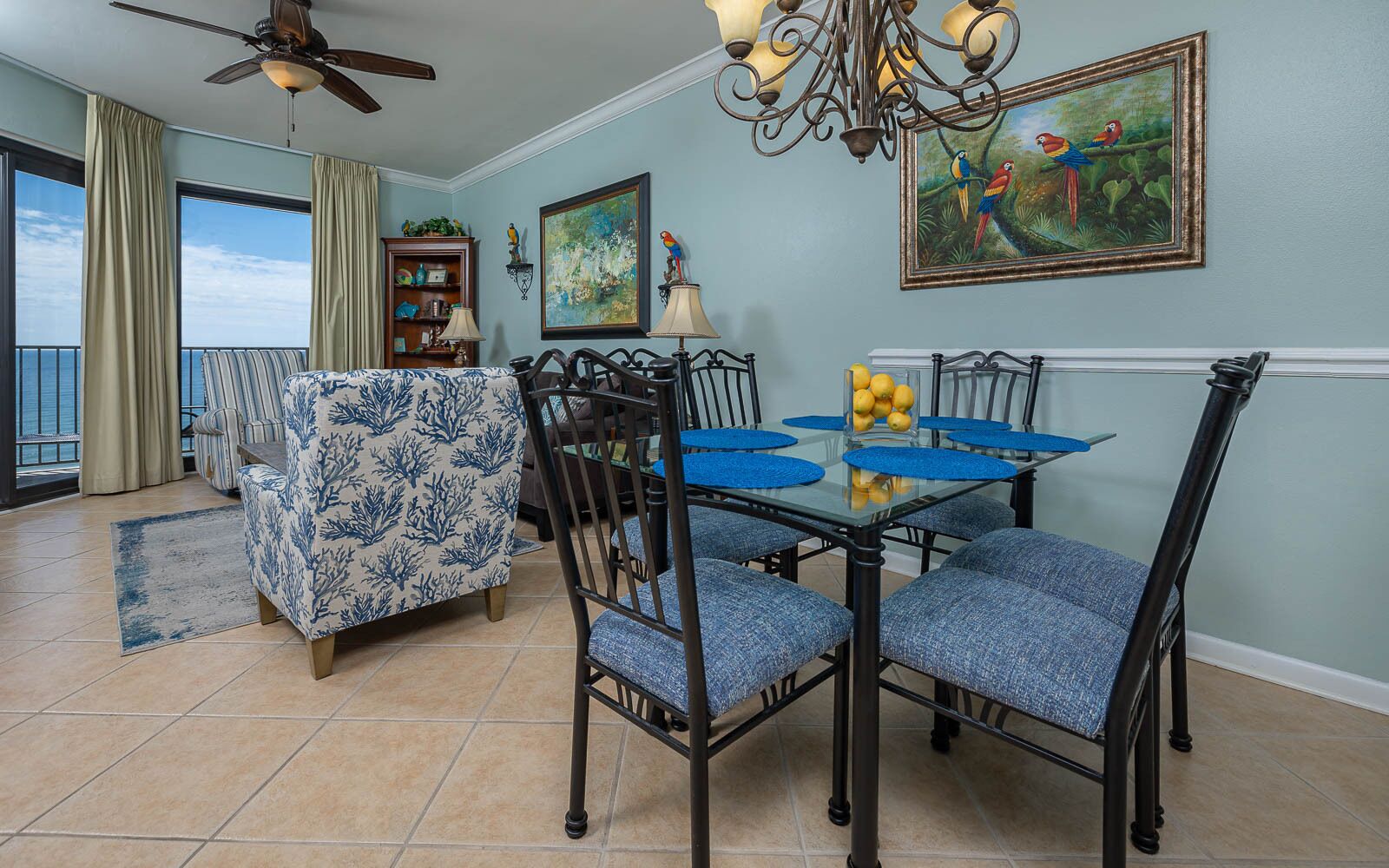 A dining area with a glass table, blue upholstered chairs, and a chandelier.