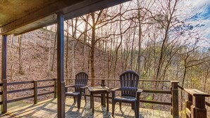 Een houten terras met Adirondack-stoelen en een tafel, met uitzicht op een bebost gebied.