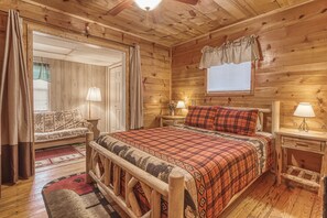 A cozy log cabin bedroom with a wooden bed, a sofa, and a window with curtains. - Bear Den, Hot Tub, “Cozy Cabin Retreat in the Smokies – Comfort & Fun for All” (Sevierville)