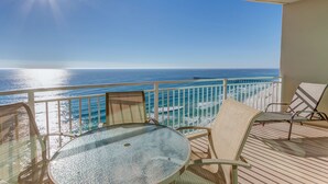 Uma varanda com mesa e cadeiras de vidro, com vista para uma praia e oceano.