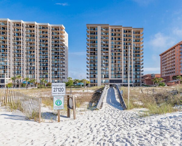 A beachfront hotel with multiple high-rise buildings, a sandy beach, and a sign indicating the address and amenities.