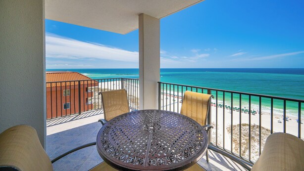 Un balcon avec une table et des chaises, donnant sur une plage et l’océan.