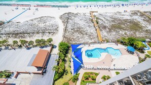 Vue aérienne d’un complexe hôtelier en bord de mer, avec une piscine, des parasols et une promenade en bord de plage.